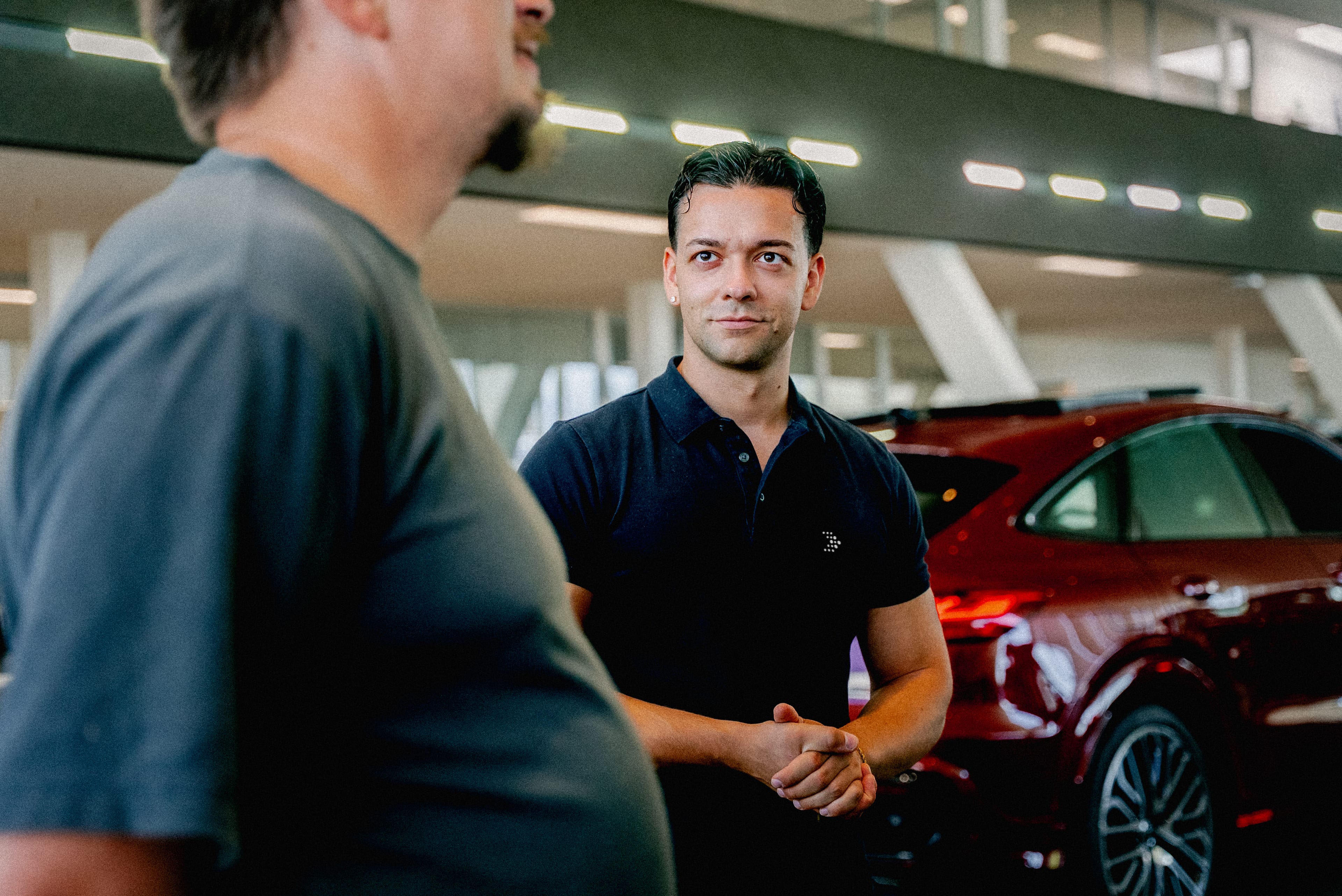 Zwei junge Männer unterhalten sich im Audi Showroom. Im Hintergrund ist das Heck eines roten Audi zu sehen und unscharf ein Audi Showroom.