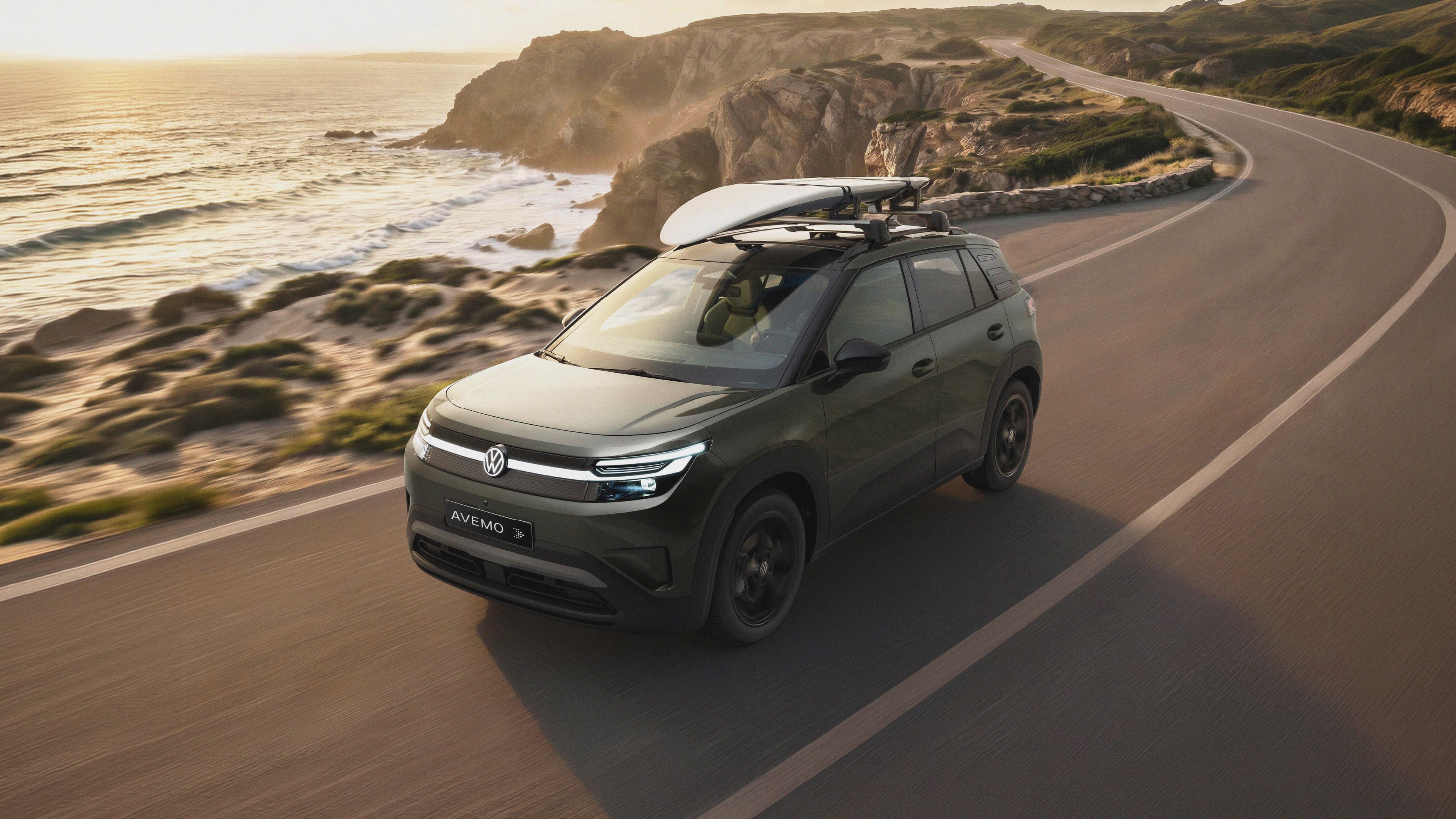 Grüner Volkswagen ID. CROSS mit Surfbrett auf einer Küstenstraße